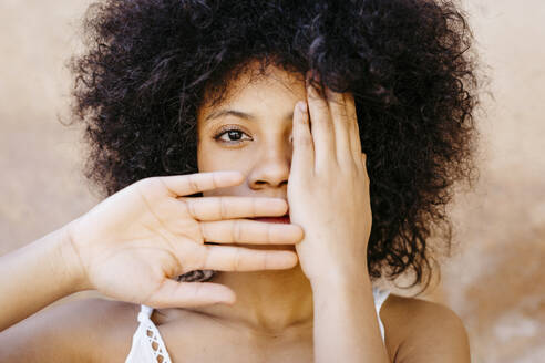 Black woman staning in front of wall, covering one eye and mouth with hands - TCEF00735