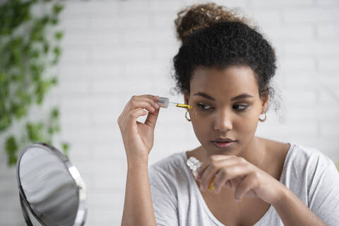 Close-up of young woman applying serum with pipette while looking in mirror at home stock photo