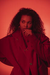 Nachdenkliche junge Frau in rotem Mantel vor orangefarbenem Hintergrund - SNF00306
