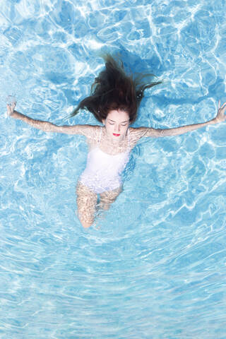 Young woman with eyed closed relaxing on swimming pool at resort during sunny day stock photo