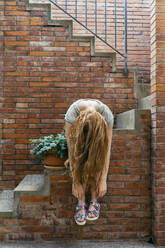 Junge Frau wirft sich die Haare, während sie auf einer Treppe sitzt - AFVF06633