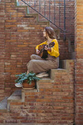 Junge Frau spielt Gitarre und sitzt auf einer Treppe - AFVF06644