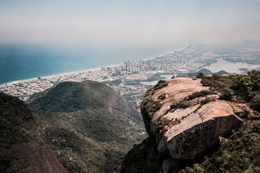 Aerial View Of Two People Sat Upon Pedra Bonita Rock With Barra Da Tijuca In Distance, Rio De Janeiro, Brazil - AAEF08903