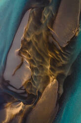 Luftaufnahme eines gelben Baches, der in den blauen Fluss Olfusa mündet, umgeben von Ackerland mit rot gefärbter Erde, die abstrakte Formen im Wasser erzeugt, Eyrarbakki, Südisland - AAEF09025