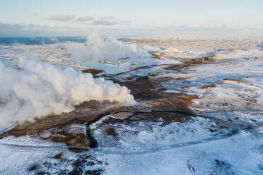 Luftaufnahme eines geothermischen Dampftopfs und eines geothermischen Kraftwerks im Hintergrund, dazwischen sind Seen mit blauem Wasser zu sehen, das von der Anlage abgeleitet wird, Gunnuhver, Reykjanes-Halbinsel, Island - AAEF09032