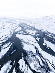Luftaufnahme eines gefrorenen Gletscherflusses, der abstrakte Muster im Schnee erzeugt, während er aus dem Thorsmork-Tal, Markarfljot, Island, herunterfließt. - AAEF09034