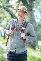 Porträt eines lächelnden Wanderers mit Hut, Brille und Rucksack im Freien - CAVF84526