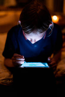 Teenager zeichnet auf einem Tablet mit hellem Bildschirm und Stift bei schwachem Licht - CAVF84535