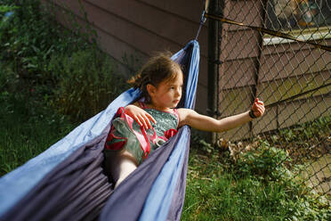 A small girl in a bright colored tutu plays in a hammock in sunshine - CAVF84595