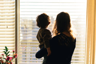 Rückansicht von Mutter und Baby stehend gegen Fenster - EYF05144