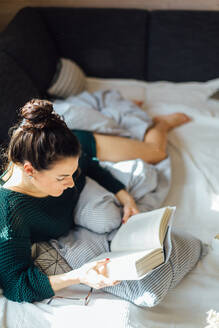 High Angle View Of Young Woman Reading Book While Lying On Bed At Home - EYF05160