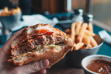 Nahaufnahme von Hand hält Burger in Platte auf dem Tisch - EYF05170