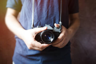 Midsection Of Man Holding Digital Camera Against Wall - EYF05173