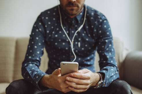 Midsection of Mid Adult Man Using Mobile Phone While Sitting On Sofa At Home - EYF05220