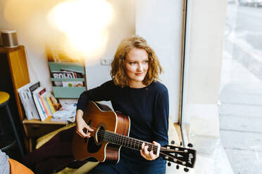 High Angle View Of Young Woman Playing Guitar By Window At Home - EYF05229