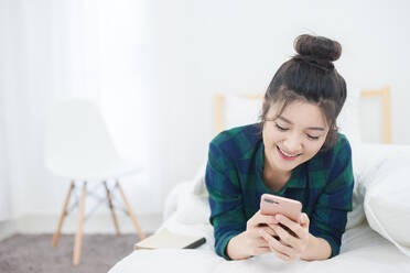 Young Woman Using Phone While Relaxing On Bed At Home - EYF05232