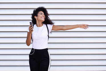 Happy Woman Listening Music While Standing Against Shutter - EYF05356