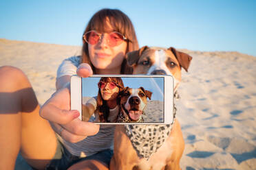 Junge Frau nimmt Selfie mit Hund durch Smart Phone am Strand gegen klaren Himmel - EYF05374