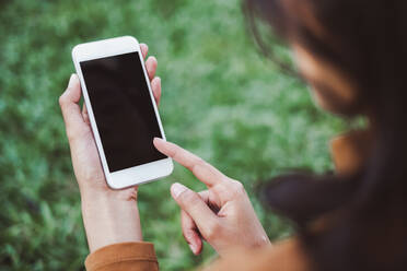 Nahaufnahme einer jungen Frau, die ein Mobiltelefon im Park benutzt - EYF05407