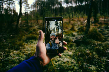 Abgeschnittene Hand eines Mannes, der ein Selfie im Wald macht - EYF05427