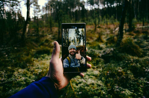 Abgeschnittene Hand eines Mannes, der ein Selfie im Wald macht - EYF05427