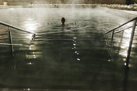 Mid adult woman swimming in hot pool at tourist resort during night stock photo