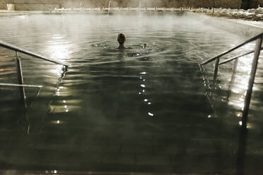 Mittlere erwachsene Frau schwimmt nachts im heißen Pool eines Ferienortes - MRRF00080