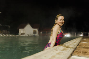 Smiling beautiful woman swimming in hot pool against sky at night - MRRF00082