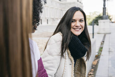 Smiling woman looking at female friends while sitting in city - ABZF03180