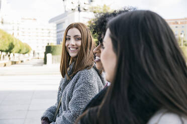 Lächelnde junge Frau, die ihre Freundinnen anschaut, während sie auf dem Stadtplatz spazieren geht - ABZF03186