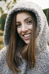 Close-up of cheerful mid adult woman wearing hood in park during winter - ABZF03201