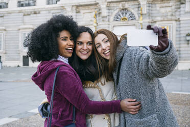 Happy female friends taking selfie with smart phone while standing against Madrid Royal Palace, Spain - ABZF03208