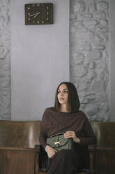 Nachdenkliche junge Frau mit Handtasche auf einem Stuhl im Designstudio sitzend - ALBF01299