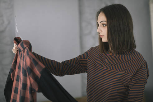 Young woman examining top while standing in clothing design studio - ALBF01301