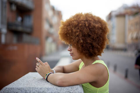 Mid adult woman with afro hair using smart phone while standing by retaining wall stock photo