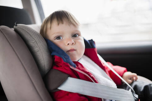 Close-up of cute baby boy sitting on car seat - RAEF02396