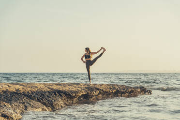 Ältere Frau übt Yoga am felsigen Strand am Abend - DLTSF00741