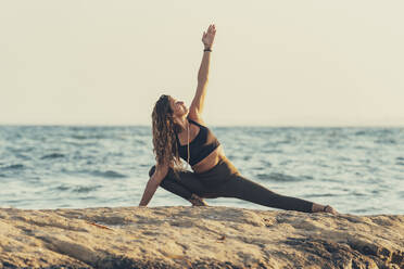 Ältere Frau übt Yoga am felsigen Strand am Abend - DLTSF00744