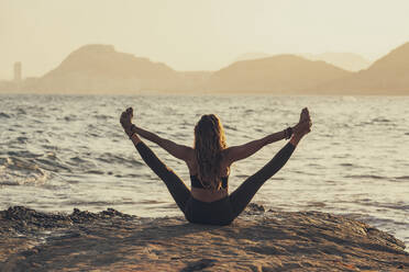 Ältere Frau übt Yoga am felsigen Strand am Abend - DLTSF00747