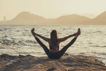 Mature woman practicing yoga at rocky beach in the evening - DLTSF00747