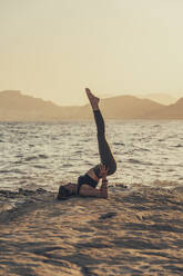 Ältere Frau übt Yoga am felsigen Strand am Abend - DLTSF00748