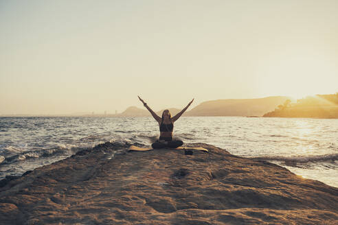 Ältere Frau übt Yoga am felsigen Strand am Abend - DLTSF00750