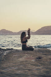 Ältere Frau übt Yoga am felsigen Strand am Abend - DLTSF00753