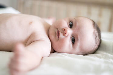Portrait of cute shirtless baby boy lying on bed at home - CAVF84950