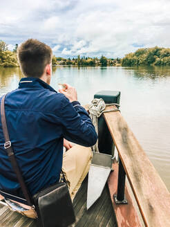 Mann trinkt ein Glas Champagner auf einem Boot und schaut auf den Fluss - CAVF84962