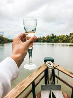 Ein Glas Champagner in der Hand am Bug eines Schiffes - CAVF84963