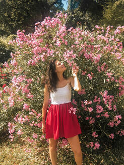 Mädchen riecht an rosa Blumen in einem roten Kleid - CAVF84965