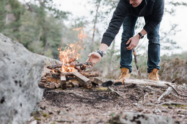 Mann legt Stöcke auf ein Lagerfeuer im Freien in Schweden - CAVF84974