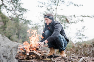 Mann legt Stöcke auf ein Lagerfeuer im Freien in Schweden - CAVF84975