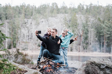Vater macht Selfies mit seinen Kindern, während er am Lagerfeuer sitzt - CAVF84980